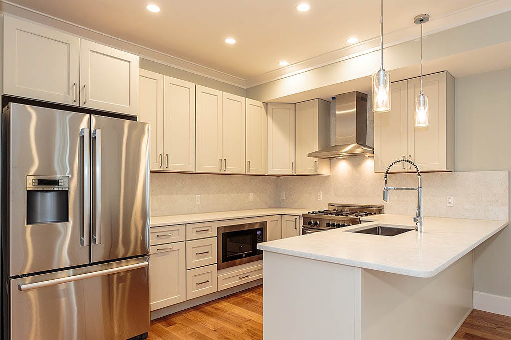 Remodeled kitchen with white granite countertops and white cabinets
